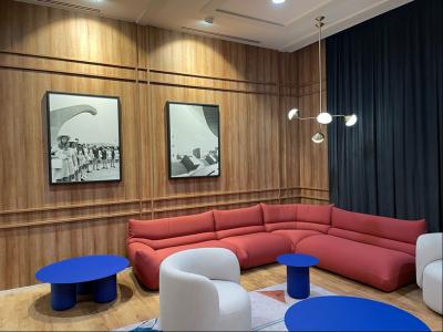 Blue coffee tables with red and white coloured lounge chairs inside a timber panelled room.