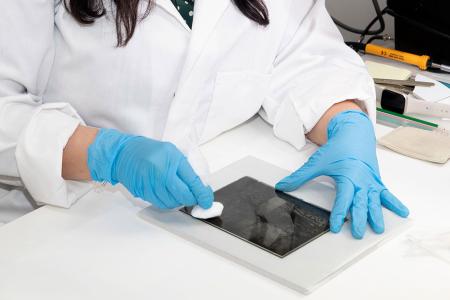 Person wearing gloves and lab coat cleaning a glass negative