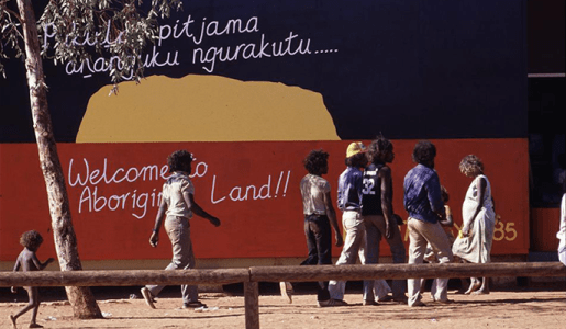 People walking past a mural with the words 'Welcome to Aboriginal land'