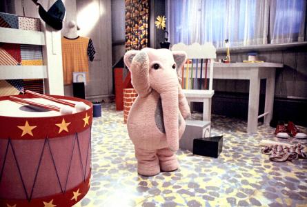 A person wearing a pink elephant costume amongst toys.