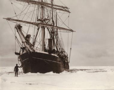 A man stands on ice below the prow of the ship Discovery 