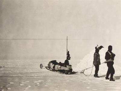 2 men towing a sled across ice.