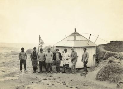 Men standing beside a hexagonal hut.