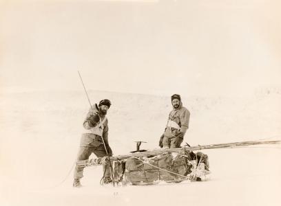 2 men stand beside a sled with supplies.
