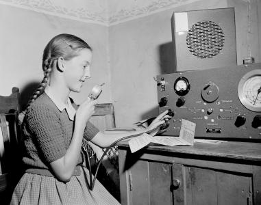 A young student speaking into a microphone attached to a large radio transceiver.