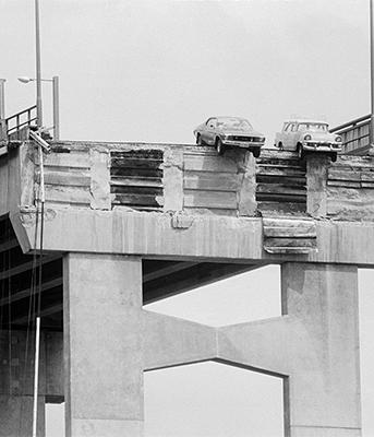 2 cars grounded on the edge of a broken bridge.
