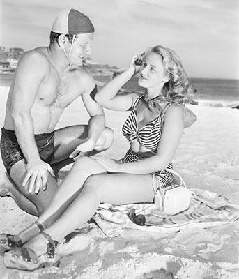 A surf life saver talking with a woman on a beach.