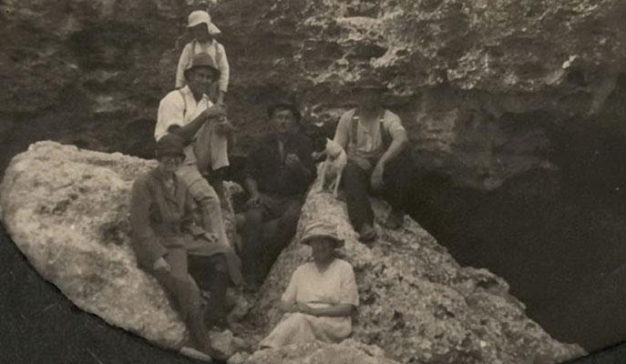 6 people sitting on a rock at the entrance to a cave