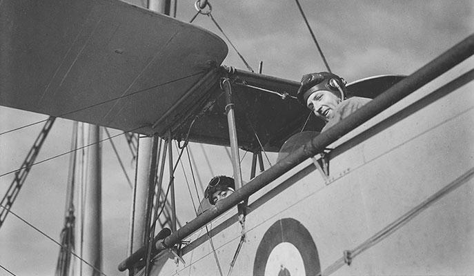 2 men looking down from the cockpits of a biplane.