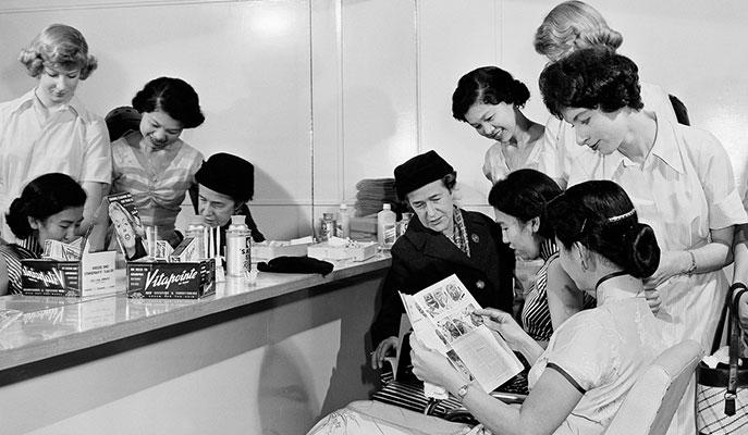 Women looking at magazines and reflected in a mirror.