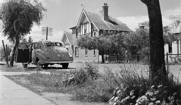 2 trees frame a 2 storey building and a car parked with an open door.