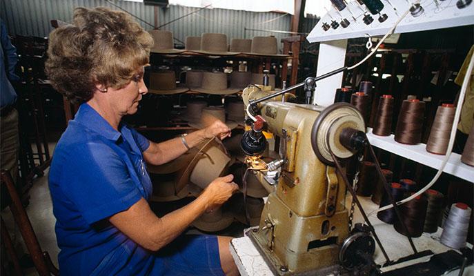 A woman sewing an Akubra hat band to a hat